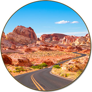 Winding road through that disappears into vibrant red Aztec sandstone rock formations and a blue sky ahead